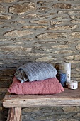 Cushions and toiletries on rough wooden bench against craggy stone wall