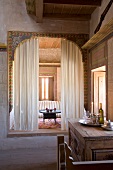 Orientalische Inszenierung in einem alten Haus - gemusterter Holzrahmen in grosser Maueröffnung mit Vorhang und Blick auf niedrigen Tablett-Tisch