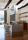 Offener Küchenraum mit Designer-Barhockern vor Edelstahl-Küchenblock, abgehängter Dunstabzugshaube und weißem Geschirr auf offenen Holzregalen