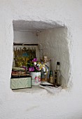 Posy of garden flowers in beaker and angel figurine in masonry wall niche
