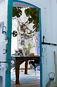 View through open door of wooden table with crockery and plant decoration in dining room