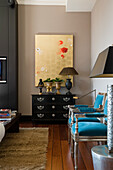 Living room with blue and silver armchairs, black chest of drawers and gold wall art