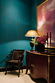 Chest of drawers with table lamp and hydrangeas in front of petrol blue wall