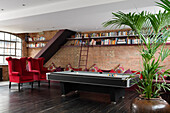 Billiard room with red armchairs, brick wall and bookshelf