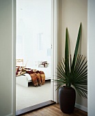 Floor vase with palm leaves next to open door showing view of bed