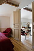 Rustic bedroom with red armchair and red throw and view of the neighbouring room