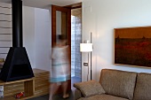 Detail of sofa and standard lamp with blurred figure of woman moving towards door