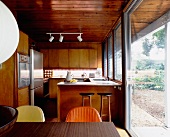 Dining area in front of open-plan kitchen with wood-panelled walls and ceiling