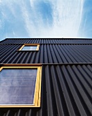 Hausfassade mit schwarzer Wellblechverkleidung und hellen Holzfenstern