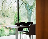 Set of designer bowls on table in front of floor-to-ceiling windows with view of garden