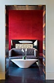 Hotellobby im italienischen Designerstil mit schiffsförmigem Tisch vor weichen Sofas und anthrazitfarbenem Schieferboden zu blutroter Wandgestaltung