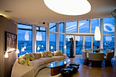 Imposanter Raum mit Wohn- und Essbereich und grosser Fensterfront in Abendbeleuchtung
