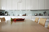 Wooden dining table in front of white fitted kitchen