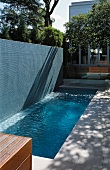 Pool with high grey concrete wall in front of contemporary villa