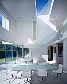 Essbereich vor dem Fensterfront, im Hintergrund führt eine Treppe mit Glasgeländer zum Obergeschoss