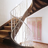 Curved staircase and wall hanging on whitewashed stone wall in traditional stairwell