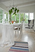 White fabric draped over dining table in loggia of white wooden house