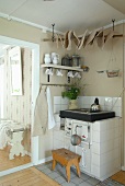 Holzschemel vor rustikalem Küchenofen mit weissen Fliesen in Zimmerecke neben Durchgang und Blick auf Sitzbank aus weißem Holz
