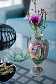 A purple flower in a decorative ornamental vase on a glass coffee table