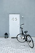 A black bicycle in a paved courtyard in front of a modern house with a unique front door