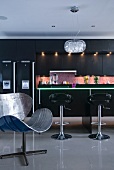 An original metal chair and a black fitted kitchen in the background with a green illuminated breakfast bar