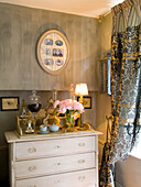 Antique chest of drawers with bouquet of flowers, patterned curtains