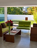 Sofa with lime green cushions and wooden frame and matching coffee table in front of floor-to-ceiling terrace windows in contemporary building