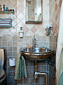 Wall tiles in earthy colours, stainless steel washbasin and open shelves