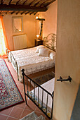 Metallbett mit weißer Bettwäsche in rustikalem Zimmer mit Terrakottafliesen