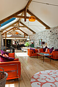 Wohnbereich mit sichtbaren Deckenbalken und Steinwand, orangefarbene Sofas