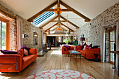 Wohnzimmer mit freiliegenden Holzbalken und Steinwänden, orangefarbenen Sofas