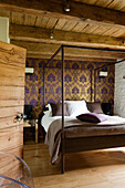 Schlafzimmer mit Himmelbett, lila-goldener Tapete und rustikalen Holzelementen
