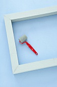 White-painted wooden frame and small paint roller on pastel blue background