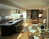 Modern, open-plan living space with long kitchen counter, dining area with glass table and children’s table in front of blackboard