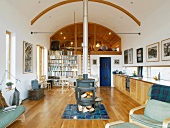 Open-plan, ecological living space with central wood-burning stove and long stovepipe up to arched ceiling
