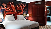 Bold, bright red mural behind snow-white bed in hotel room with ensuite bathroom
