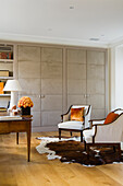 Room with classic armchairs, flowers, cupboards, wooden floor and cowhide rug