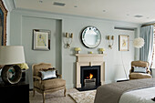 Bedroom with fireplace, upholstered armchairs and wall mirror