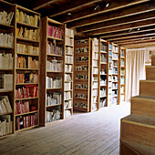 Library with ceiling-high bookshelves under wooden beamed ceiling, wooden floor