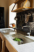 Kitchen with marble sink, black mosaic splashback and hanging kitchen utensils