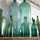 Glass bottles and jars in green on wooden shelf in front of unplastered wall