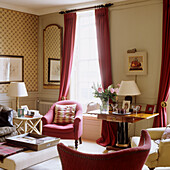 Living room with red armchairs, floor-length curtains and bouquet of flowers on side table