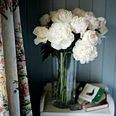 White peonies in glass vase, curtain with floral pattern