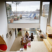 Wohnraum mit offener Treppe und Dachterrasse mit Liegestühlen und Stadtblick