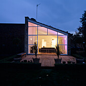 Modern living room with glass front and wooden terrace at dusk