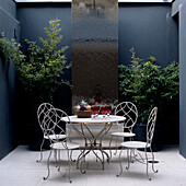 Modern patio with waterfall wall, delicate metal chairs and plants in black pots