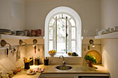 Kitchen with arched window, shelves and worktop with kitchen utensils