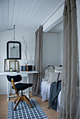 Schlafzimmer mit Tisch, Stuhl, Bett mit Zierkissen, weißen Wänden, weißer Holzdecke und Vintage-Deko