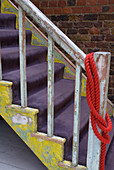 Old wooden staircase with scraped-off paint and purple velour carpet on treads