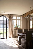 Open, arched metal door in country-house dining room with loose-covered chairs